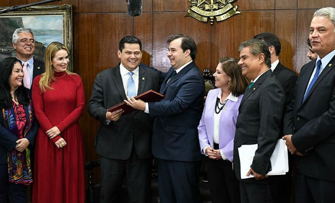 O presidente do Senado, Davi Alcolumbre, recebe de Rodrigo Maia o texto da proposta, observado pelos senadores Rose de Freitas, Major Olimpio, Daniella Ribeiro, Nelsinho Trad e Sérgio Petecão e por deputados | Roque de Sá/Agência Senado